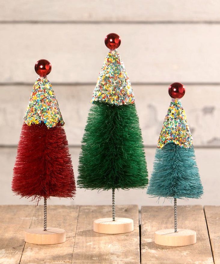 three small christmas trees with colorful decorations on top of each one, sitting on a wooden table