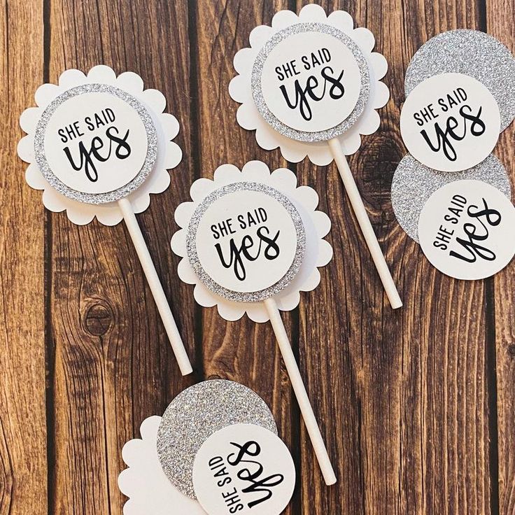 six white and silver cupcake toppers with the words she said yes on them