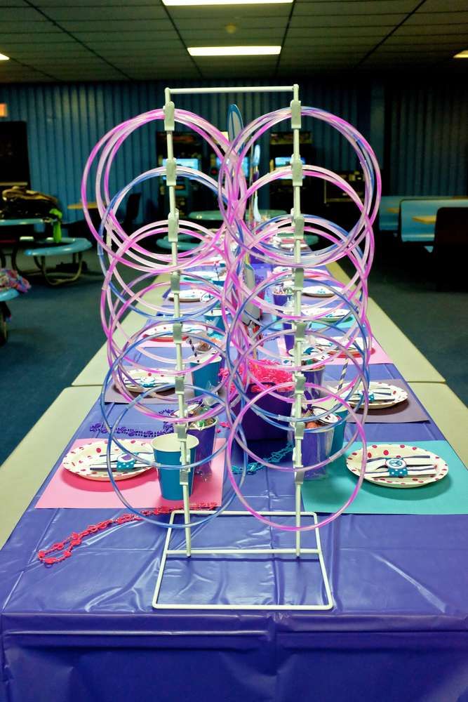 a purple table topped with lots of plates and cups covered in pink streamers on top of a blue table cloth