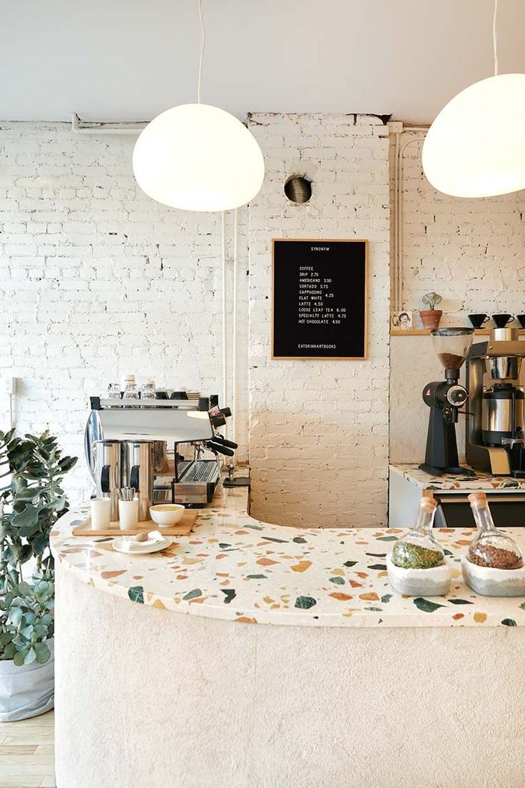 a coffee shop with white brick walls and potted plants on the counter, along with two hanging lights