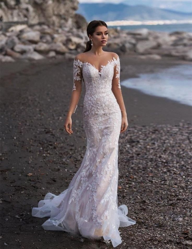 a woman standing on top of a beach next to the ocean wearing a wedding dress