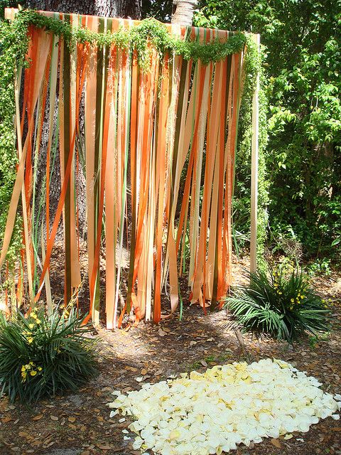 an outdoor wedding ceremony with orange ribbons and flowers on the ground in front of a tree