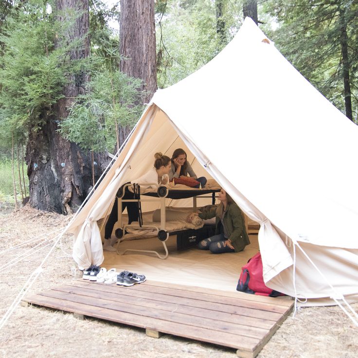 two people are sitting in a tent on the ground next to a picnic table and chairs