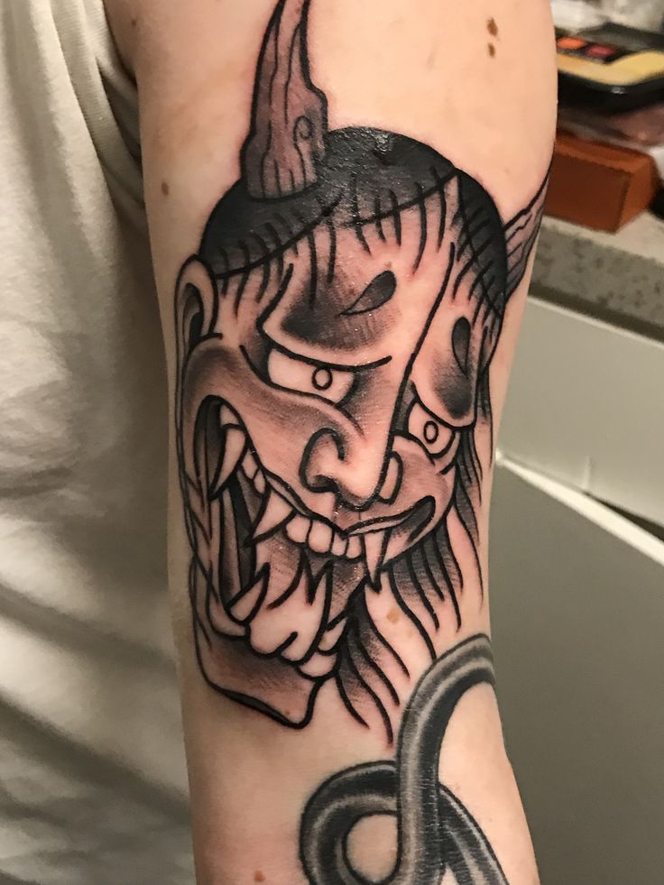 a man with a tattoo on his arm and head is wearing a demon's mask