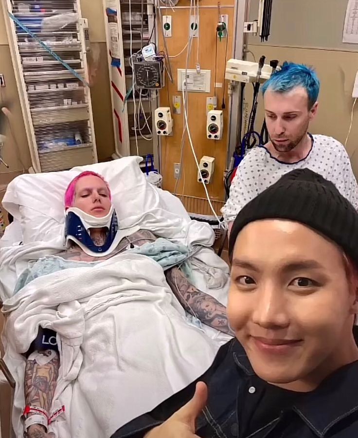 two people in a hospital room with one giving the thumbs up and another pointing at the camera