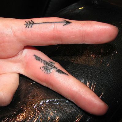 a person's left hand with an arrow tattoo on it and the other finger