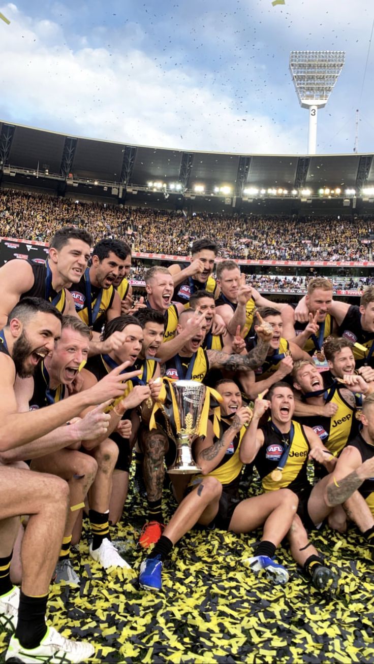 a group of men standing next to each other on top of a field holding a trophy