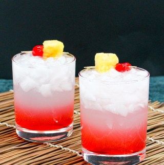 two glasses filled with drinks sitting on top of a bamboo mat next to each other