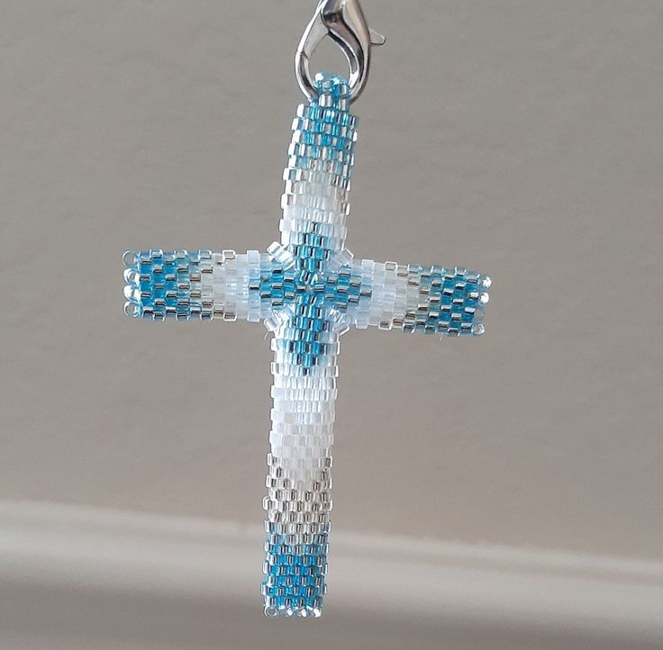 a blue and white beaded cross hanging from a silver plated chain on a wall