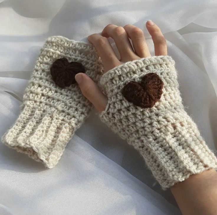 a woman's hand is holding up a crocheted glove with a brown heart on it