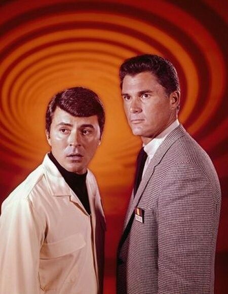 two men standing next to each other in front of a red and yellow spiral background