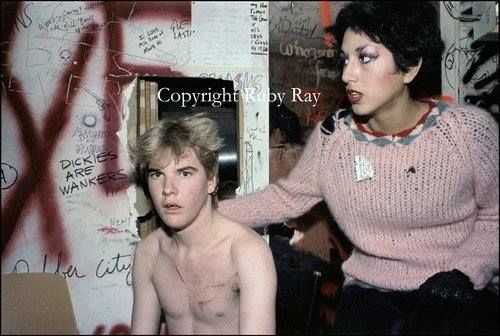 two young people are posing in front of a wall with graffiti on it and one is brushing his hair