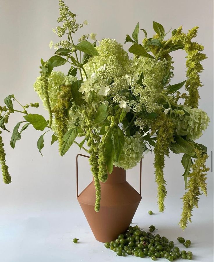 a vase filled with lots of green flowers on top of a white table next to peas