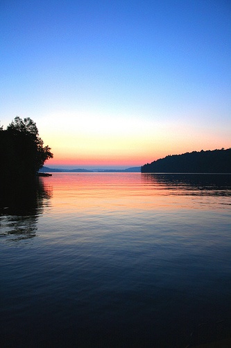 the sun is setting over water with trees in the foreground