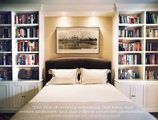 a bed with white sheets and pillows in front of bookshelves filled with books