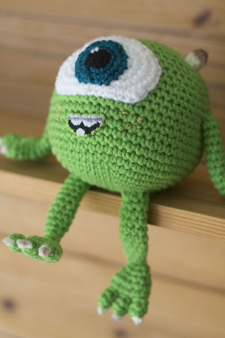 a crocheted green stuffed animal sitting on top of a wooden shelf next to a wall