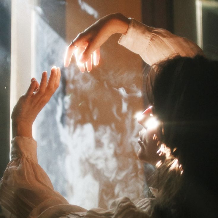 a person reaching out their hand to touch the light coming from behind them in front of a window