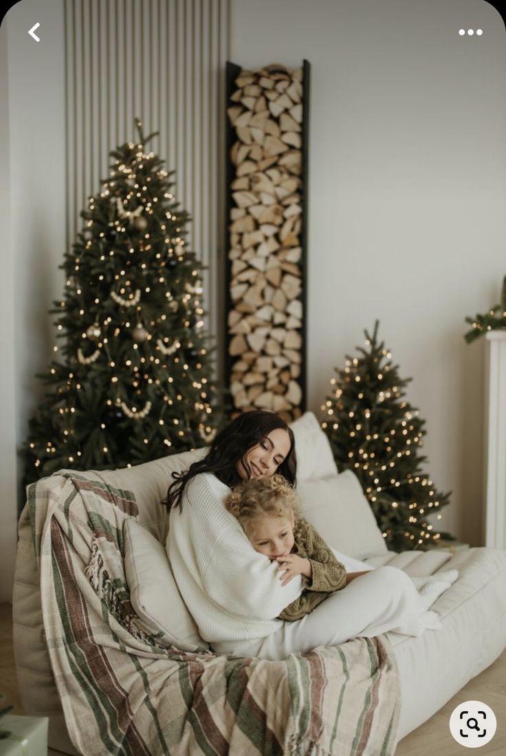 a woman and child sitting on a couch in front of christmas trees with lights around them