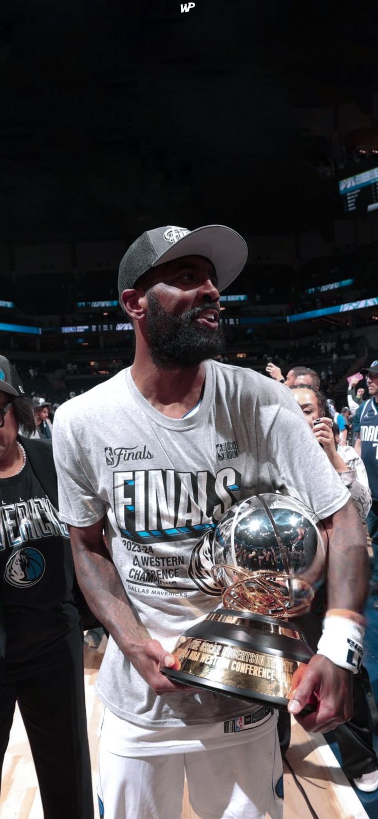 a man holding a trophy while standing on top of a basketball court in front of other people