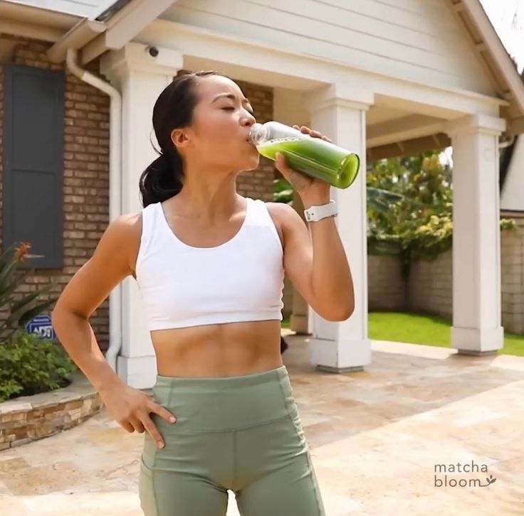 a woman standing in front of a house drinking from a green bottle