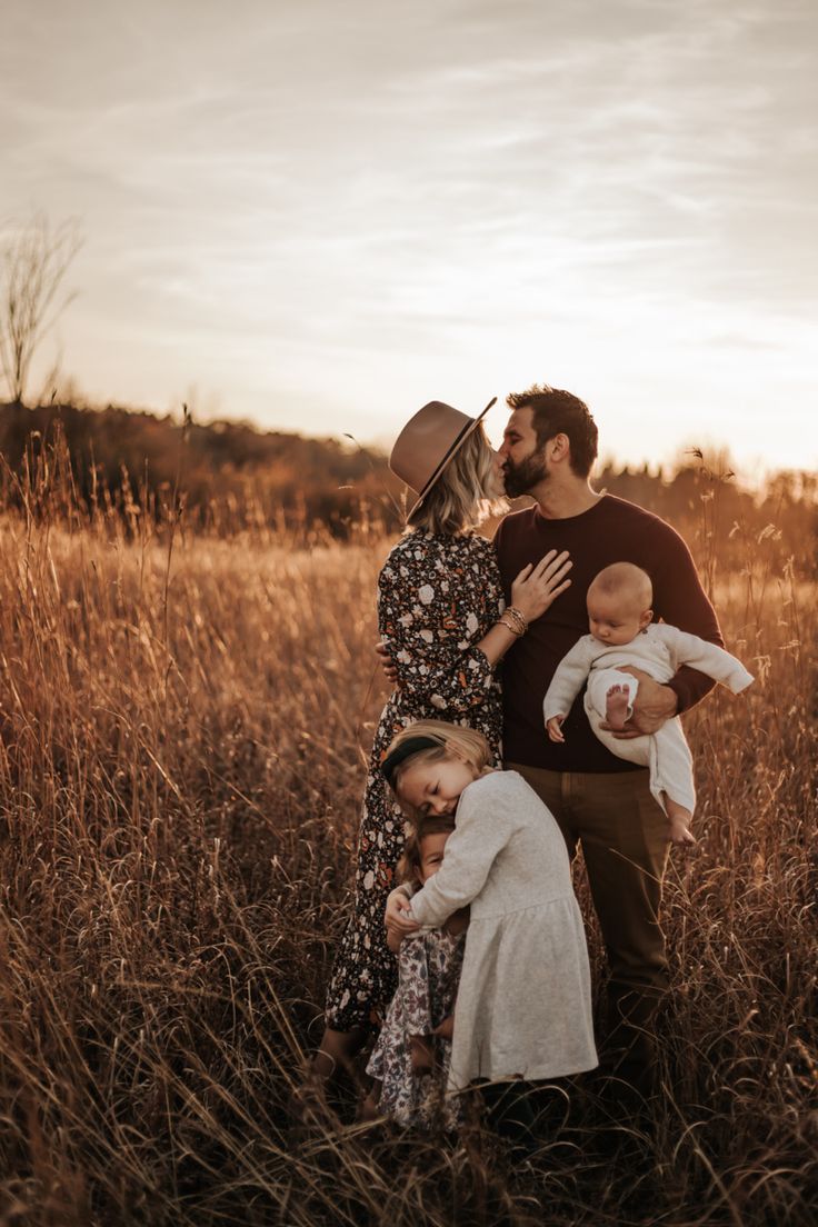 a family standing in tall grass at sunset with their baby girl and dad holding her