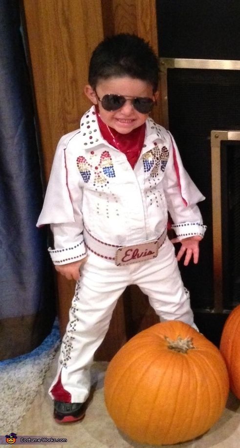 a young boy dressed in elvis clothing standing next to two pumpkins on the floor