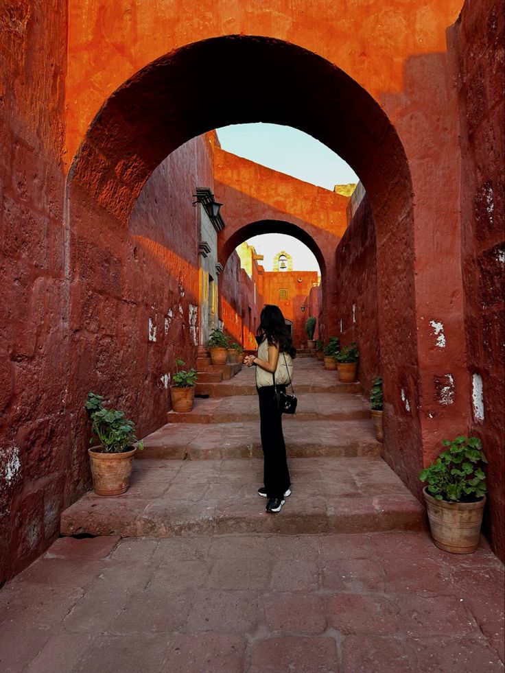 a woman is standing in an alley between two buildings with arches and potted plants