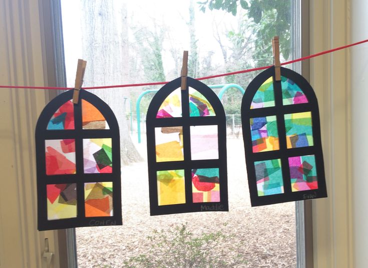 three stained glass windows hanging on a line in front of a window with clothes pins