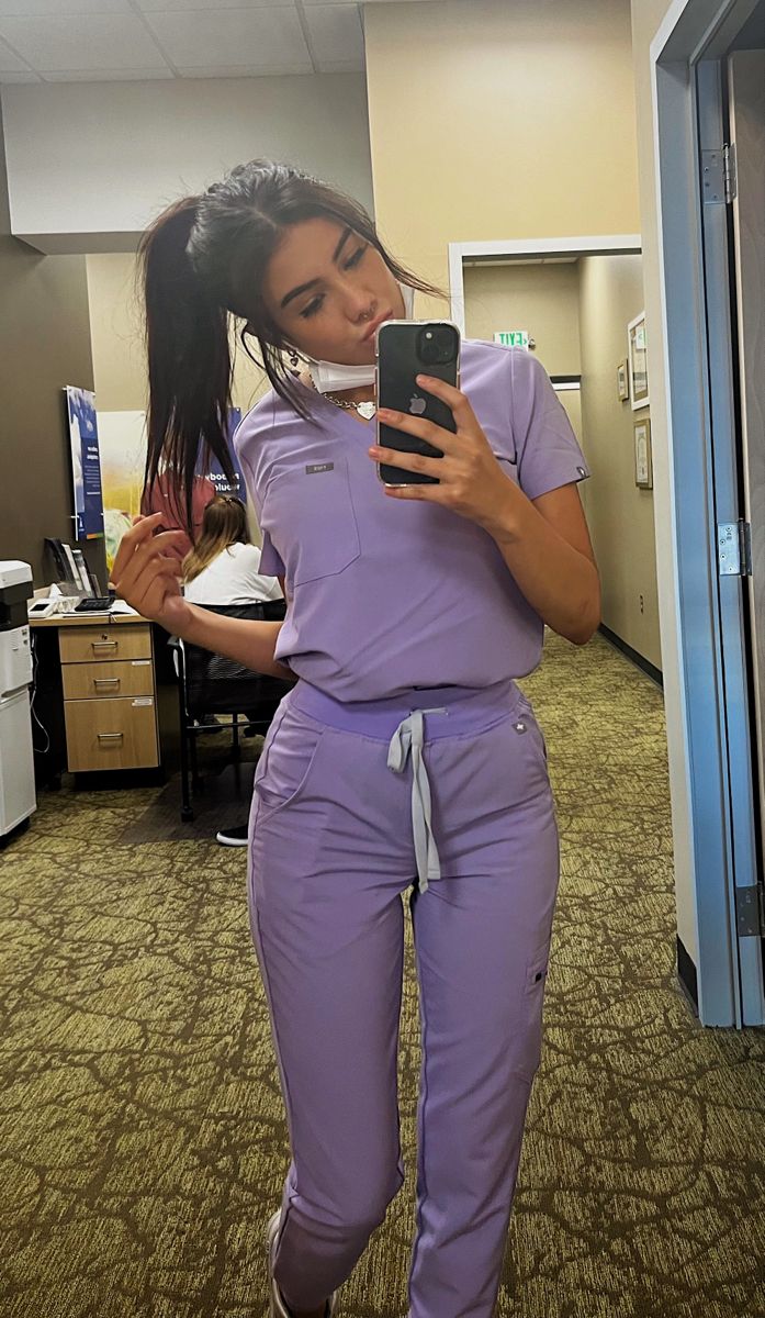 a woman in scrubs is looking at her cell phone while standing in an office