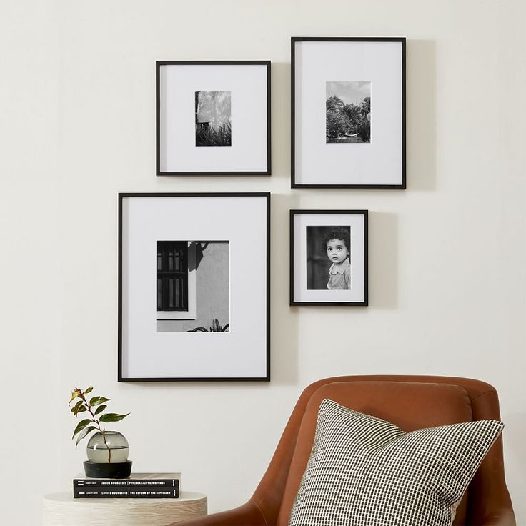 four black and white pictures hang on the wall above a chair with a pillow, vase, and plant