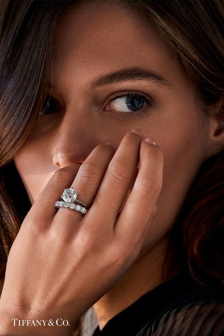 a woman wearing a diamond ring and holding her hand up to her face with both hands