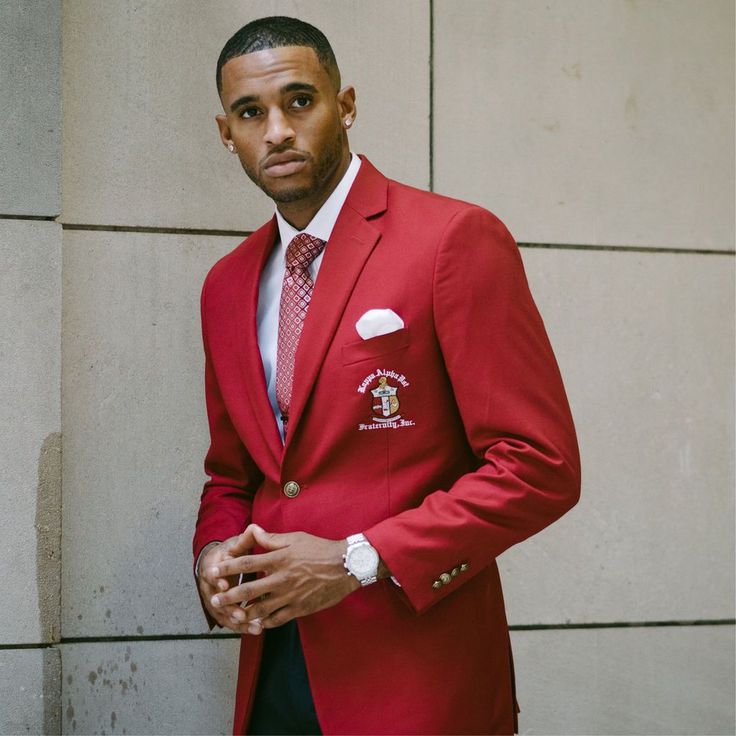 a man in a red jacket and tie standing next to a wall wearing a watch