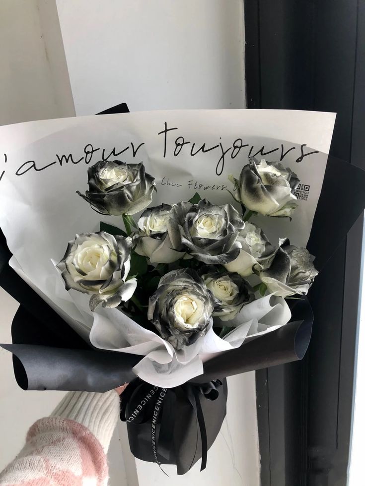 a bouquet of white and black roses is held by someone's hand in front of a window