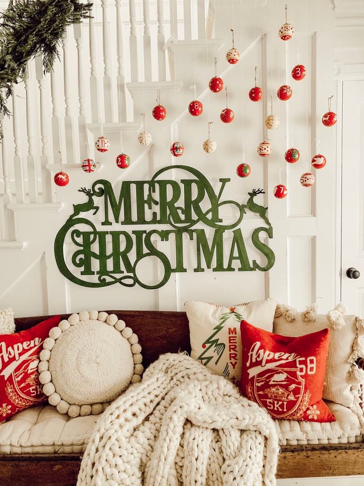 a couch covered in blankets and pillows next to a merry christmas sign on the wall