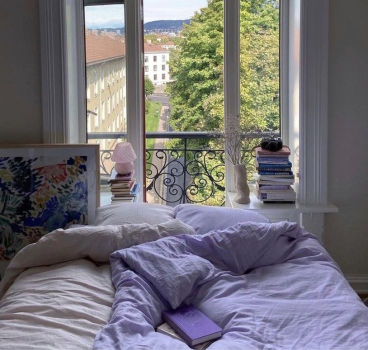 an unmade bed sitting in front of two windows with books on top of it