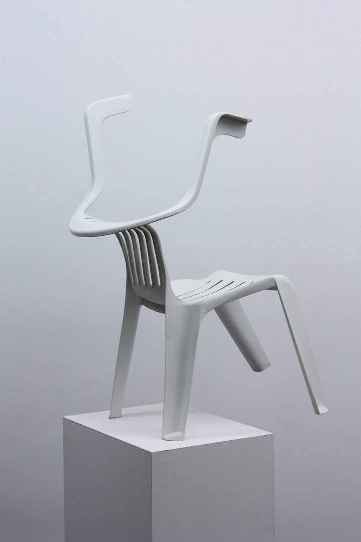 a white plastic chair sitting on top of a square block in front of a gray wall