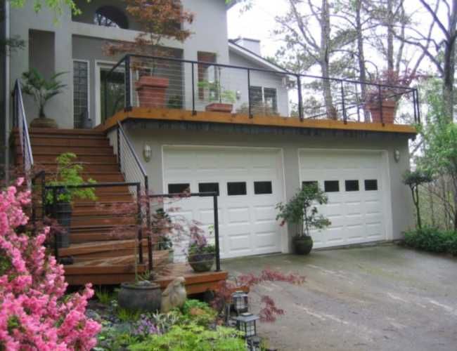 a house with two garages and stairs leading to the second floor, surrounded by flowers