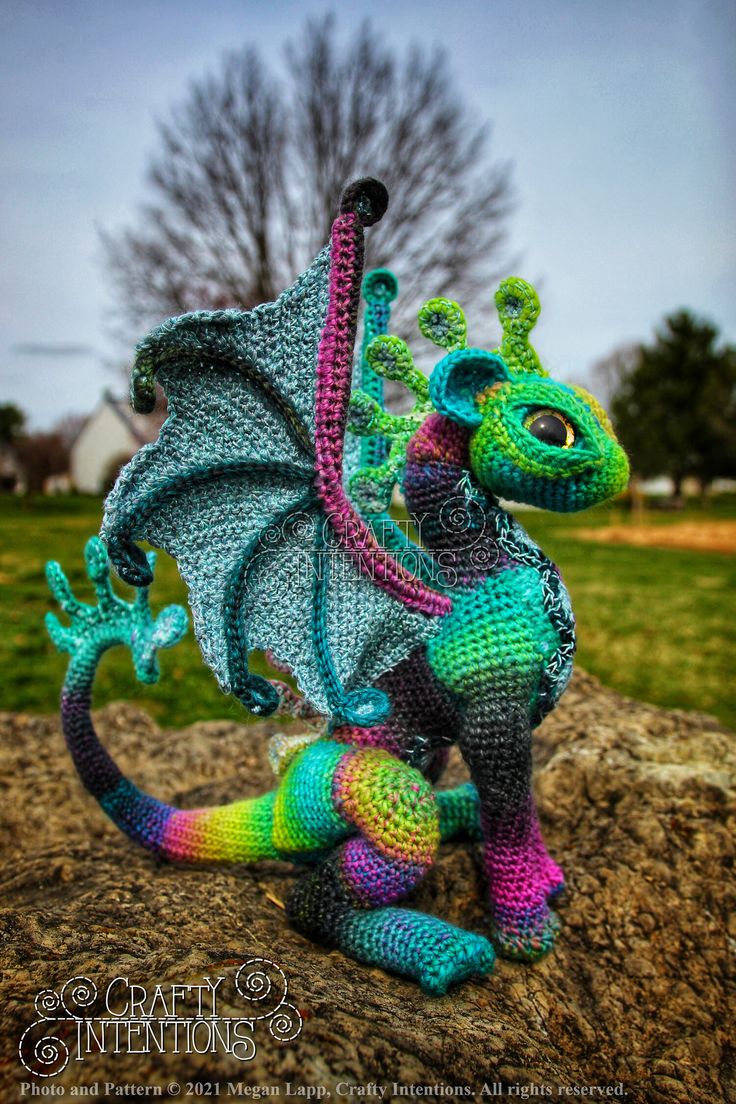 a crocheted dragon sitting on top of a rock