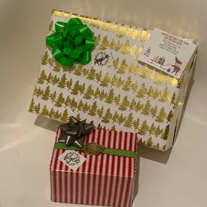 two wrapped presents sitting on top of a white table next to each other with green bows