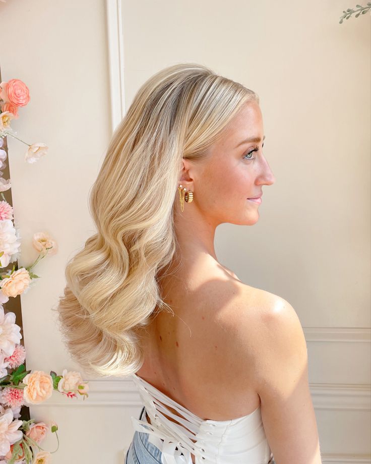 a woman with long blonde hair standing in front of a flowered wall and looking off to the side