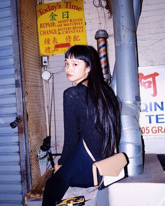 a woman sitting on the ground next to a metal pole with a sign in the background