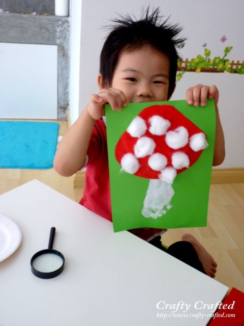 a young boy holding up a piece of paper with mushrooms on it