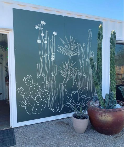 a large cactus plant sitting next to a green wall with white drawings on it's side