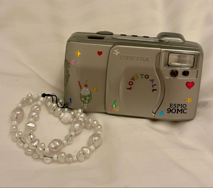 a camera with a chain attached to it on top of a white bed sheet next to a bracelet