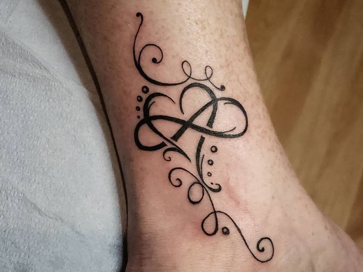 a tattoo on the foot of a woman with an initial letter and swirls in black ink