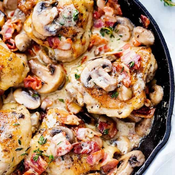 a skillet filled with chicken and mushrooms on top of a white cloth next to a fork