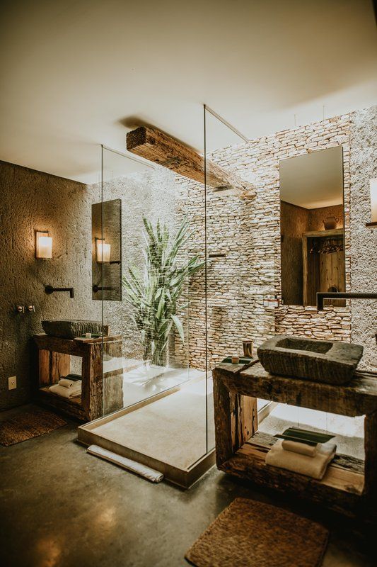 a bathroom with a stone wall and glass shower stall, sink and mirror in it