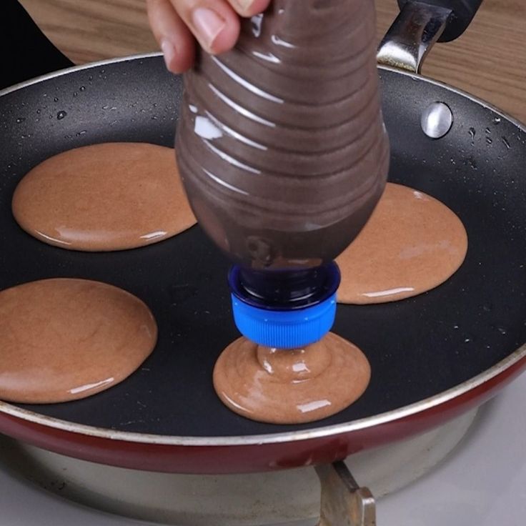 someone is pouring chocolate sauce on top of pancakes in a frying pan with blue handles