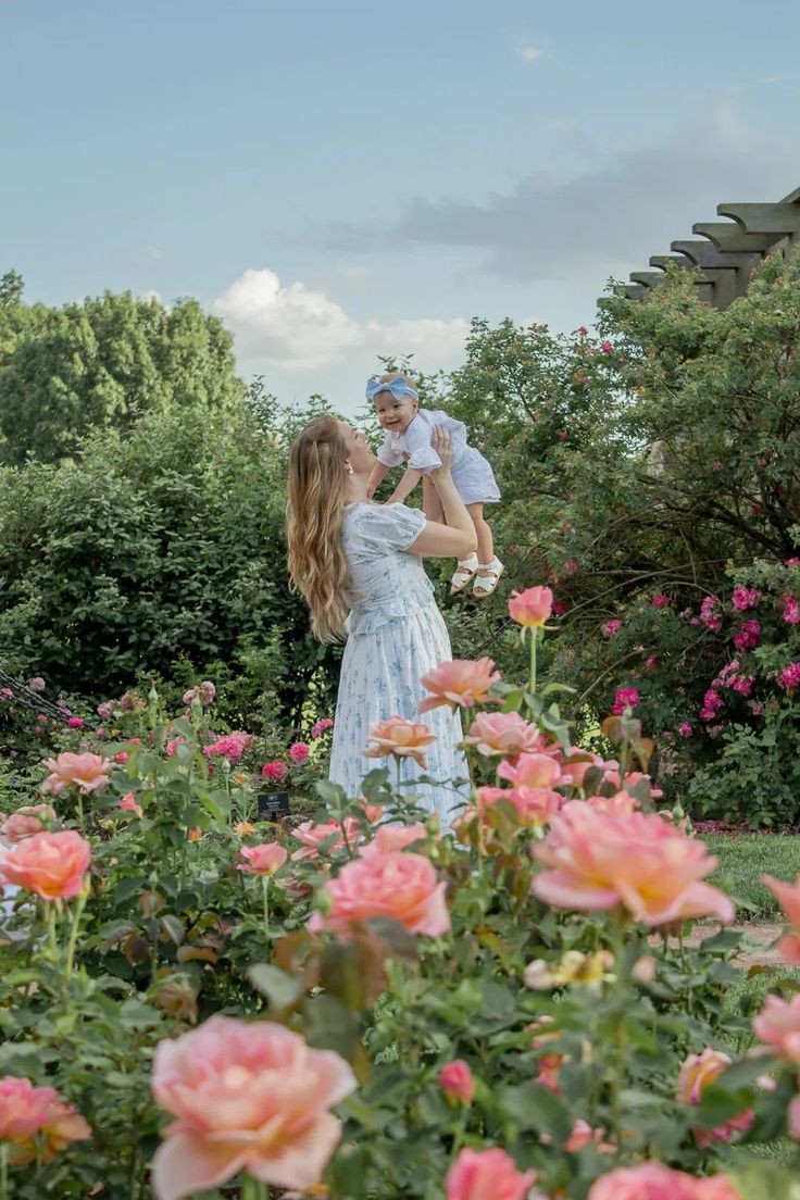 a woman holding a baby in her arms while standing next to pink flowers and trees