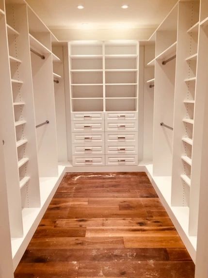 an empty walk - in closet with white shelving and wooden flooring is shown